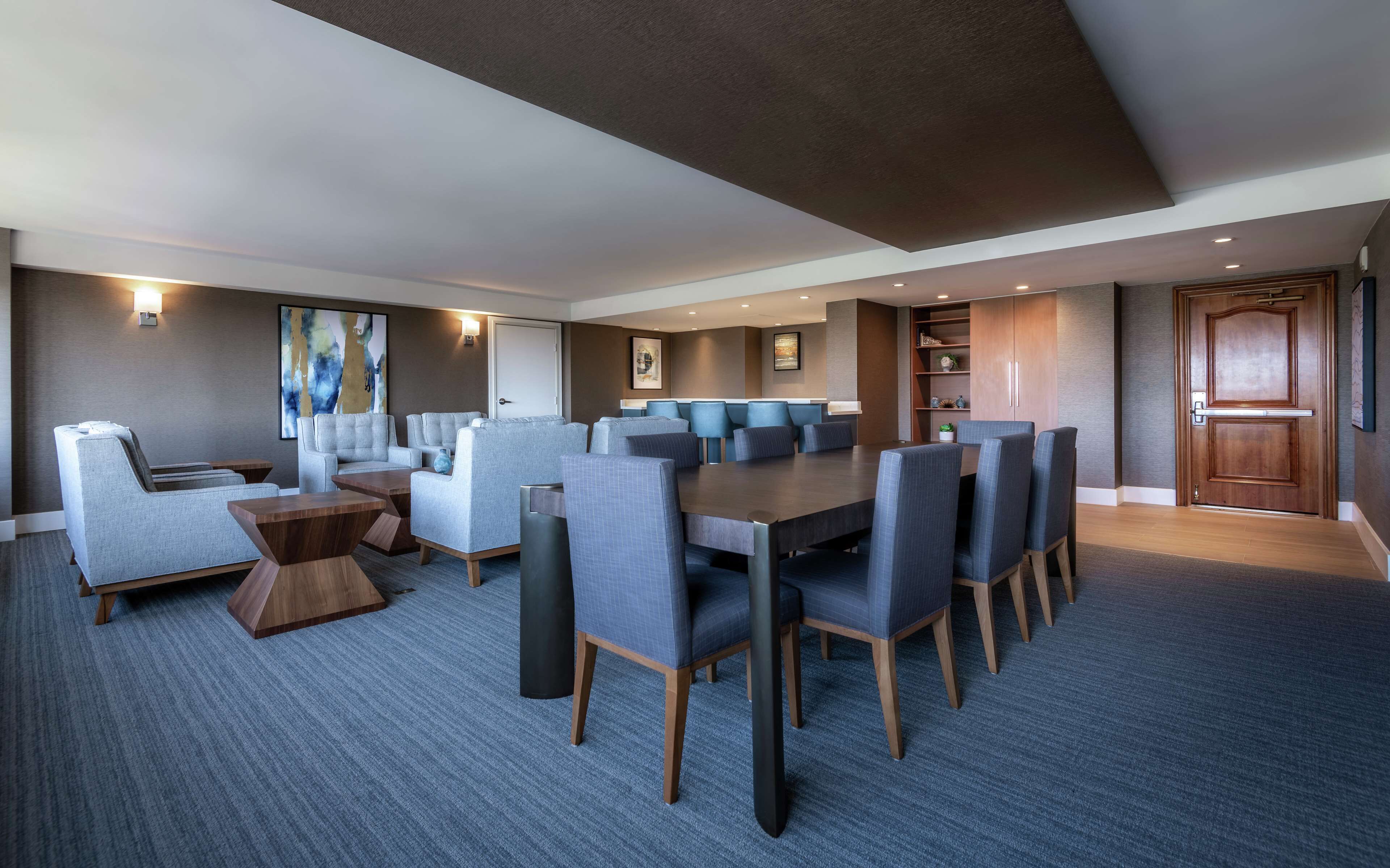 A modern hotel room with a large dining table, comfortable seating, and a cozy seating area with a fireplace.