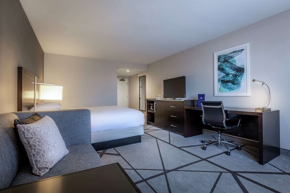 Une chambre d’hôtel avec un lit, un bureau, une chaise, une lampe, une télévision et un tableau au mur.
