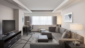 Una habitación de hotel moderna con una televisión de pantalla plana, un sofá, un escritorio con una silla y una lámpara.