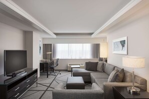 A modern hotel room with a flat-screen TV, a sofa, a desk with a chair, and a lamp. - DoubleTree by Hilton Los Angeles - Norwalk (Norwalk)