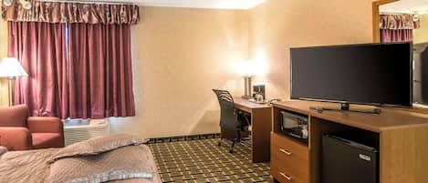 A hotel room with a bed, a desk, a television, a refrigerator, and a chair.