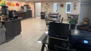 A modern kitchen with a coffee station, dining area with tables and chairs, and a business center with computers and a printer.