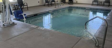 An indoor swimming pool with clear water, a lifeguard chair, and a pool ladder.