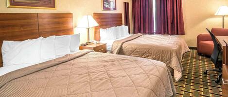 A hotel room with two beds, a wooden headboard, a desk with a chair, a telephone, and a window with curtains.