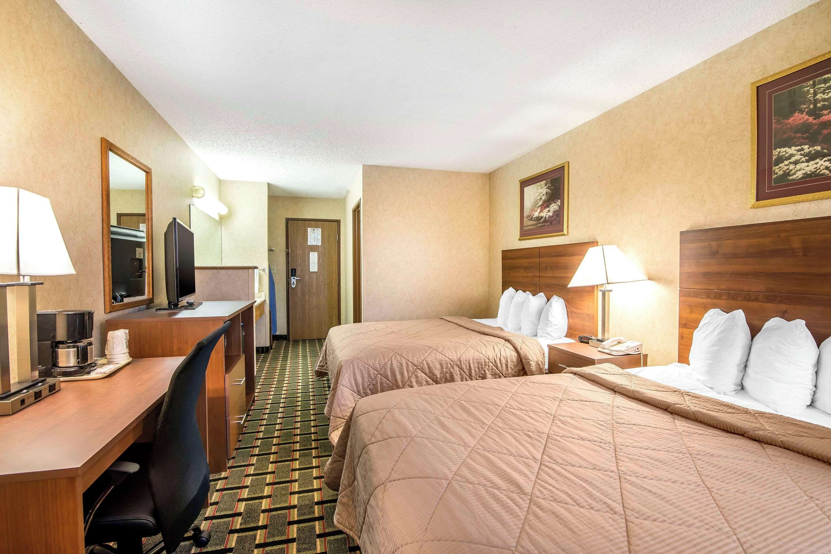 A hotel room with two beds, a desk with a computer, a TV, and a mirror.