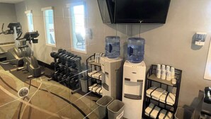 A hotel fitness center with exercise equipment, water dispensers, and a TV mounted on the wall. - Quality Inn Raton, NM (Raton)