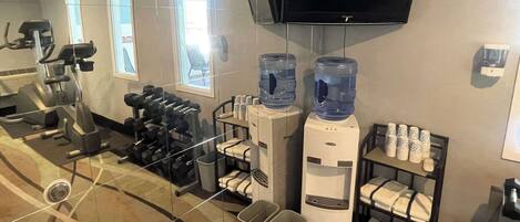 Un gimnasio de hotel con equipo de ejercicio, dispensadores de agua y un televisor montado en la pared.