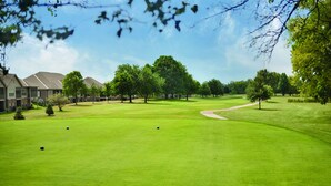 A well-maintained golf course with a clear path, surrounded by trees and residential buildings.