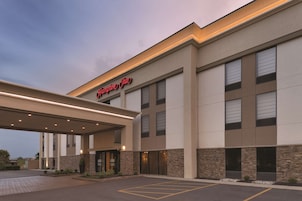 Entrada moderna de hotel con zona de estacionamiento techada y un cartel que dice "Hampton Inn".
