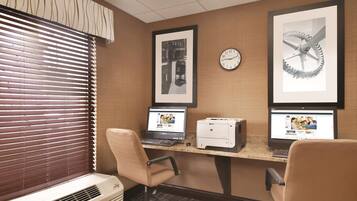 Un'area reception di un hotel con due postazioni computer, un orologio e opere d'arte incorniciate appese al muro.