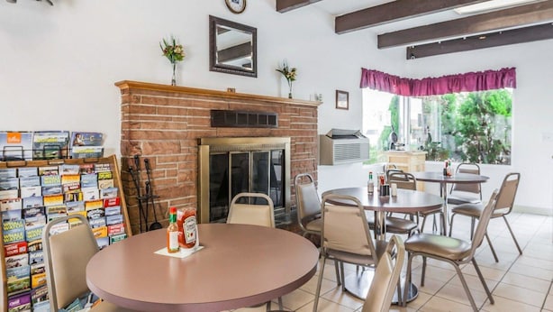 Un comedor con chimenea de ladrillo, un reloj en la pared y una ventana con vista a follaje.