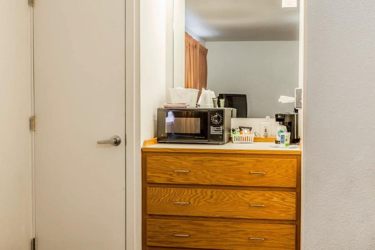 A hotel room with a wooden dresser, a microwave, and a mirror with lights above it.
