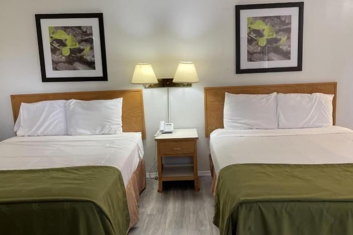 A hotel room with two beds, a nightstand with a lamp, and two framed pictures on the wall.
