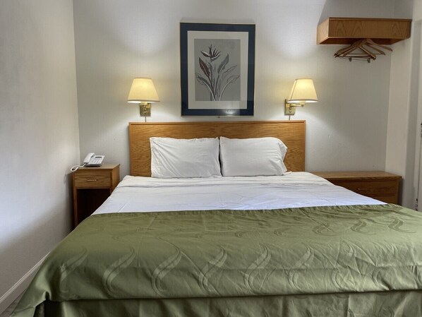 A neatly made bed with a green bedspread, two bedside lamps, a wooden headboard, and a framed artwork above the bed.