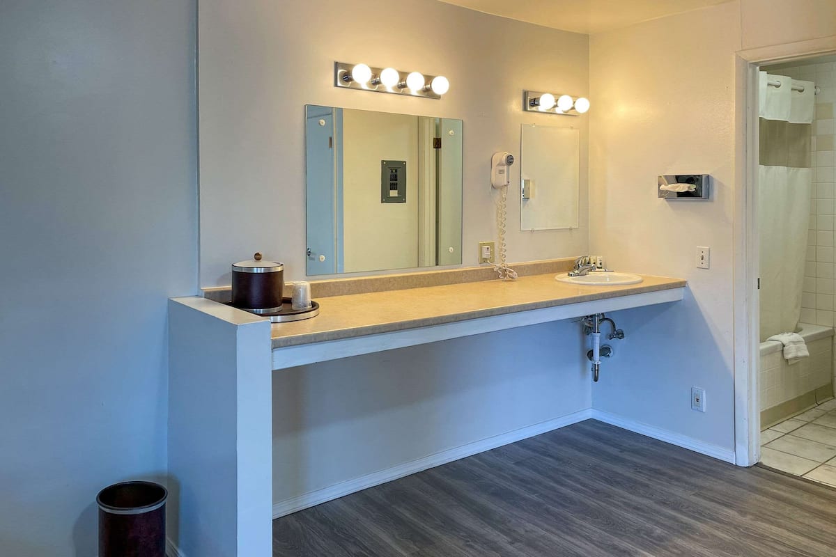 A bathroom with a vanity, a mirror with lights, a hairdryer, and a trash can.