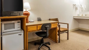 Habitación de hotel con un escritorio de madera, una silla de oficina negra, un televisor, un microondas y un refrigerador.