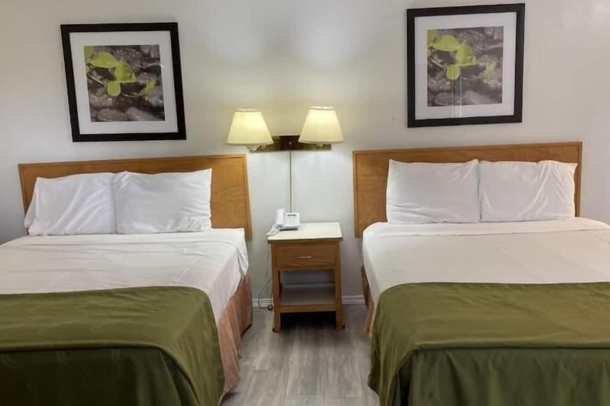 A hotel room with two beds, a nightstand with a lamp, and two framed pictures on the wall.