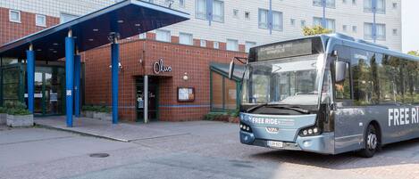 Un edificio moderno con un toldo azul en la entrada y un autobús con la leyenda