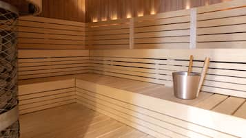 Una sauna con listelli di legno, una panca e un catino di metallo con un bastone di legno.