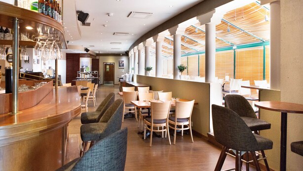 A restaurant with a bar area, multiple tables and chairs, and large windows allowing natural light. - Scandic Helsinki Aviapolis (Vantaa)