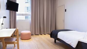 A modern hotel room with a bed, a desk, a chair, a television, and a window with curtains.