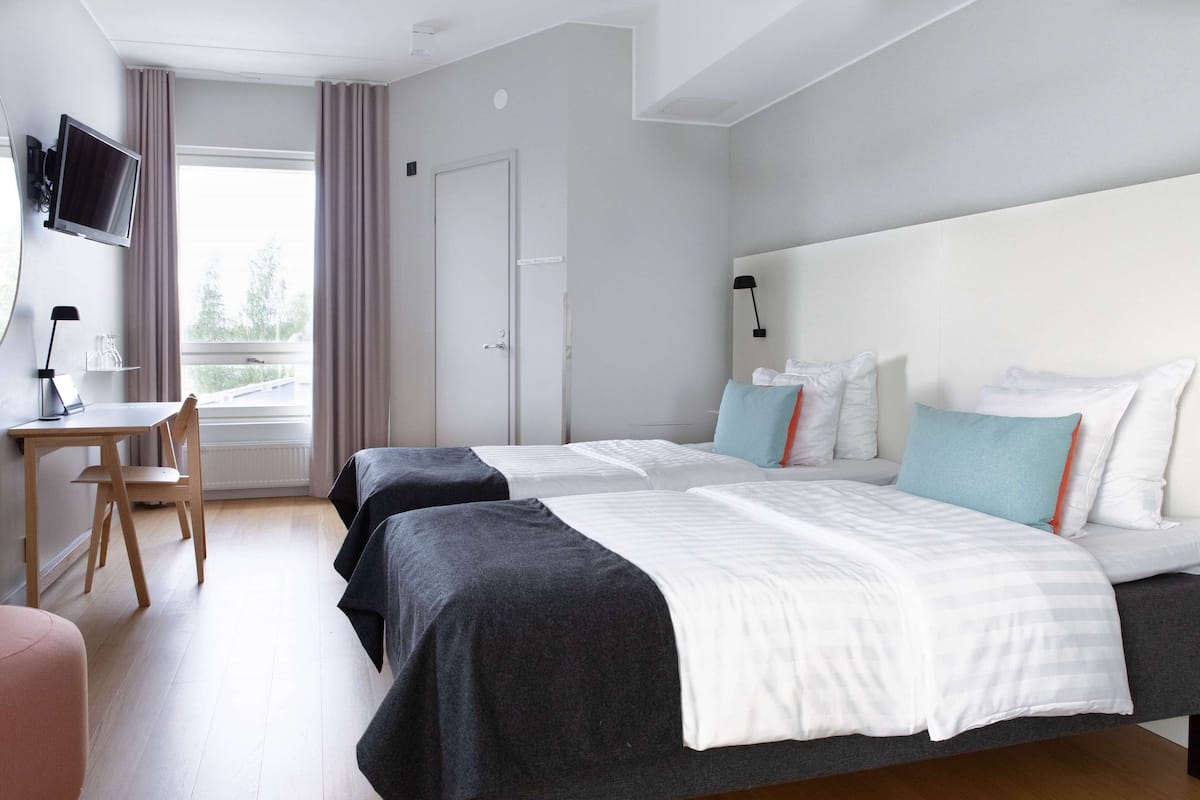Habitación de hotel con dos camas, un escritorio, una silla, un televisor y una ventana con cortinas.