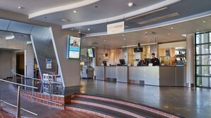 A modern hotel lobby with a reception desk, a bar area, and a staircase leading to an upper level. - Scandic Helsinki Aviapolis (Vantaa)