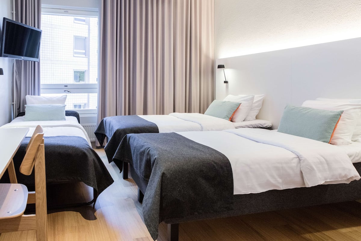 Habitación de hotel con dos camas, un escritorio, una silla, un televisor y una ventana con cortinas.
