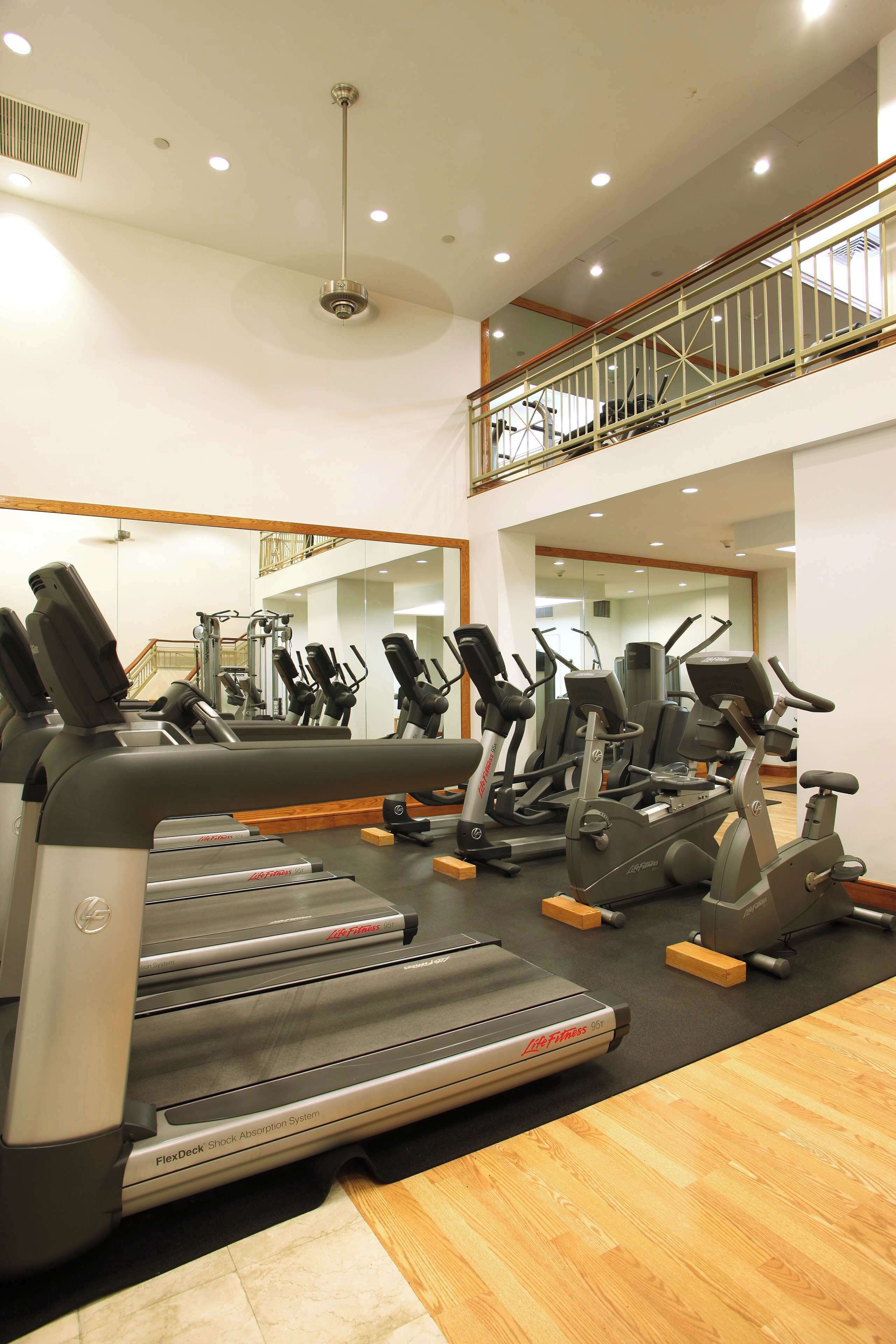 A gym with various cardio machines, a mirrored wall, and a wooden floor.