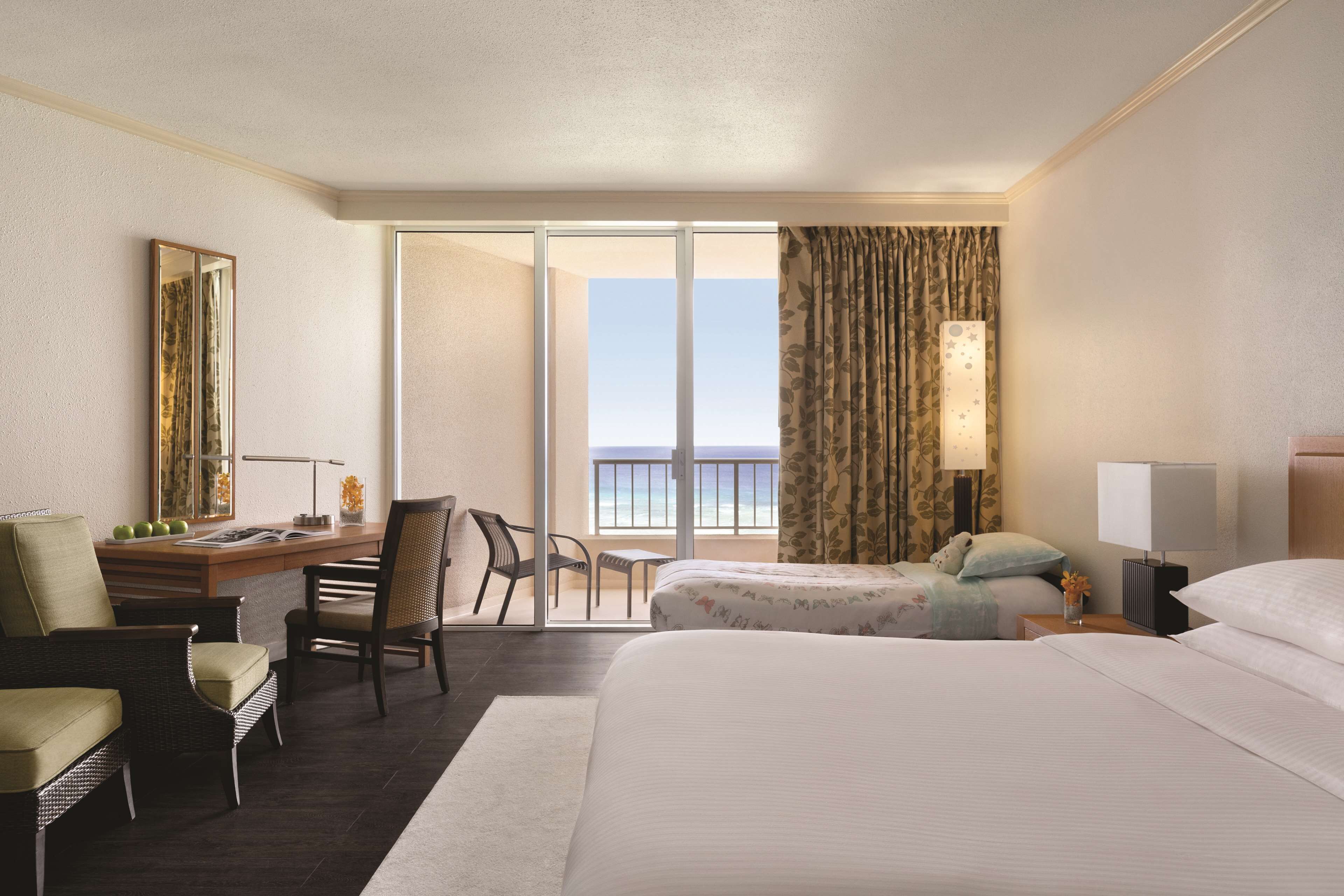 A hotel room with a large bed, a desk with a chair, a small table, and a balcony with a view.