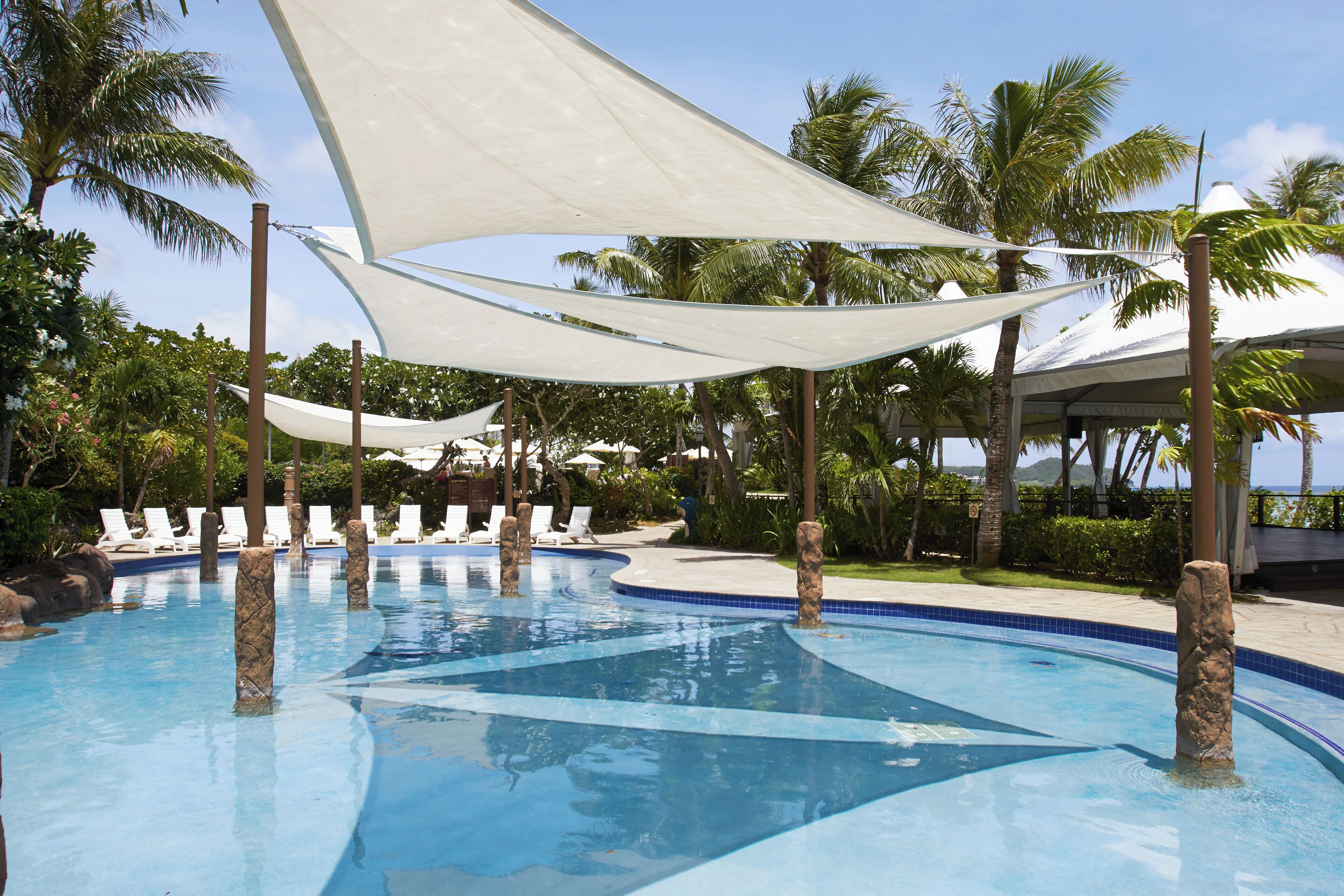 Una piscina con sillones de descanso y palmeras.