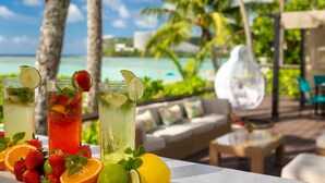 A table with three glasses of tropical drinks, surrounded by fresh fruits and a view of a beach and palm trees. - Hyatt Regency Guam (Tamuning)
