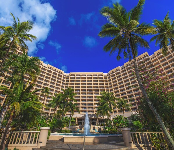 A hotel with a central fountain, surrounded by palm trees and a clear blue sky.