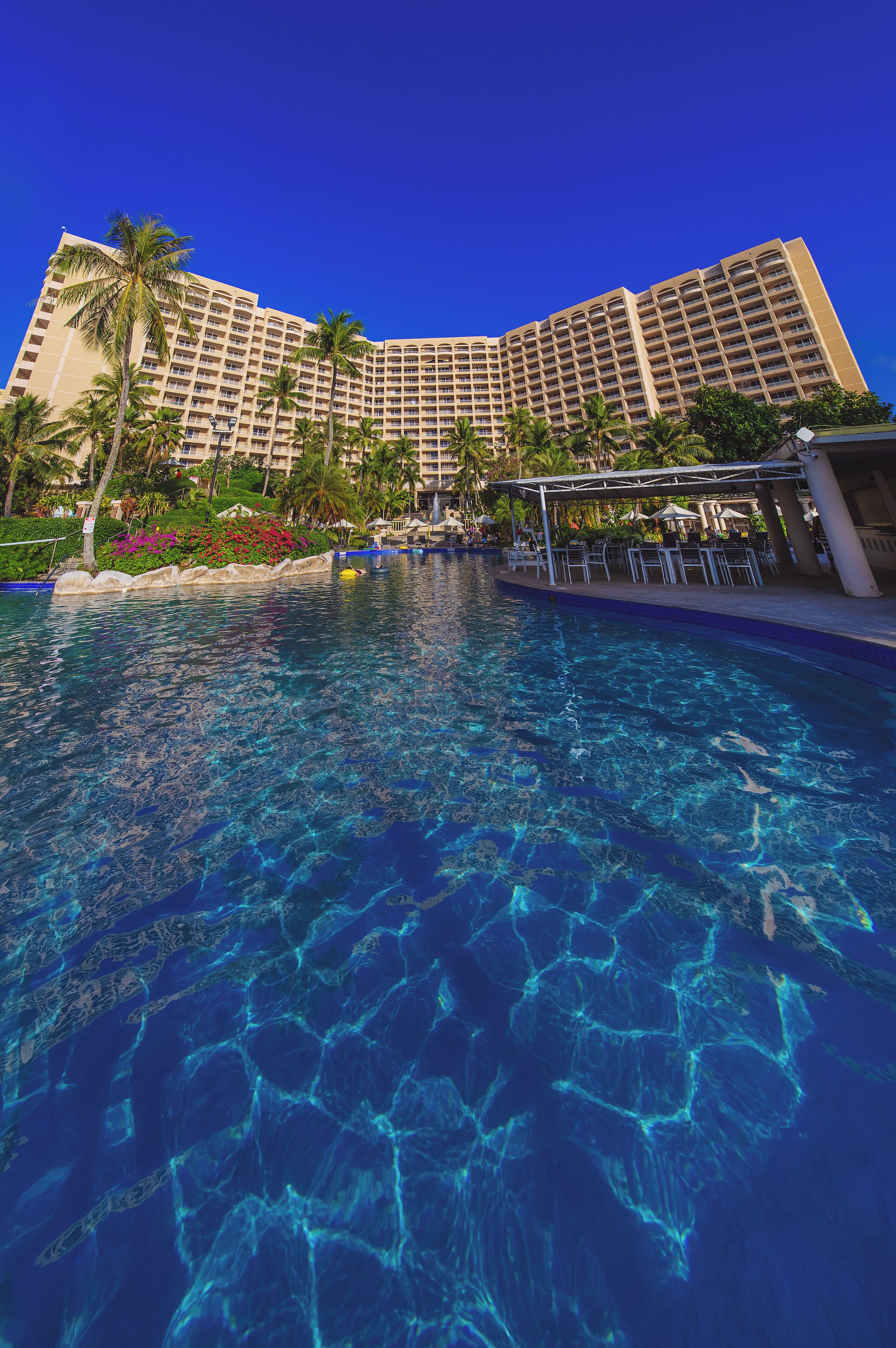 A hotel with a large pool, palm trees, and a clear blue sky.