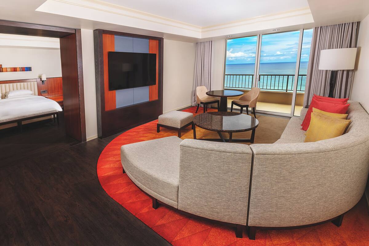 A hotel room with a bed, a sofa, a coffee table, and a balcony with a view of the sea.