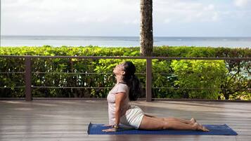 A person performing a yoga pose on a blue mat outdoors with a view of the ocean and greenery in the background.