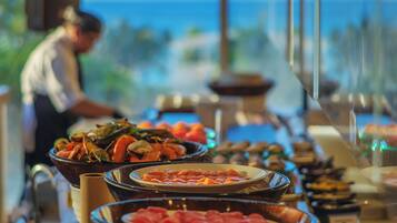 A buffet table with various dishes, a person in the background, and a view of the ocean through large windows.