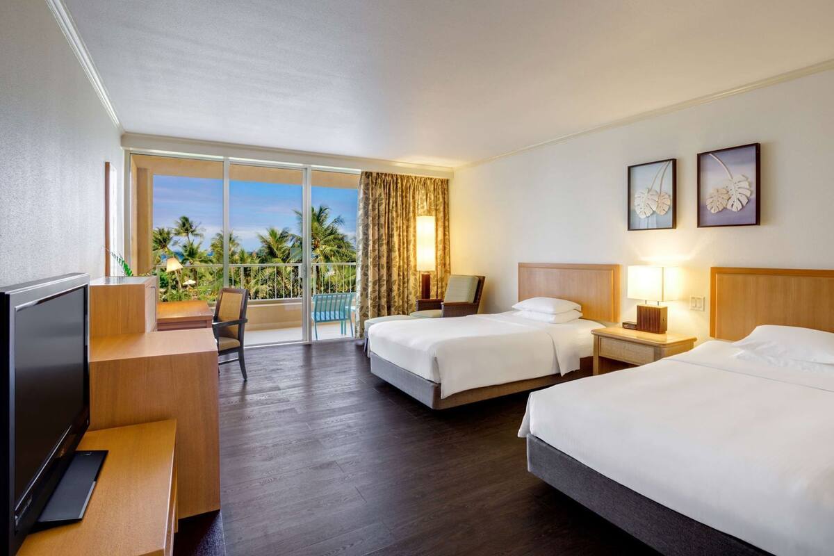 A hotel room with a balcony, two beds, a TV, and artwork on the wall.
