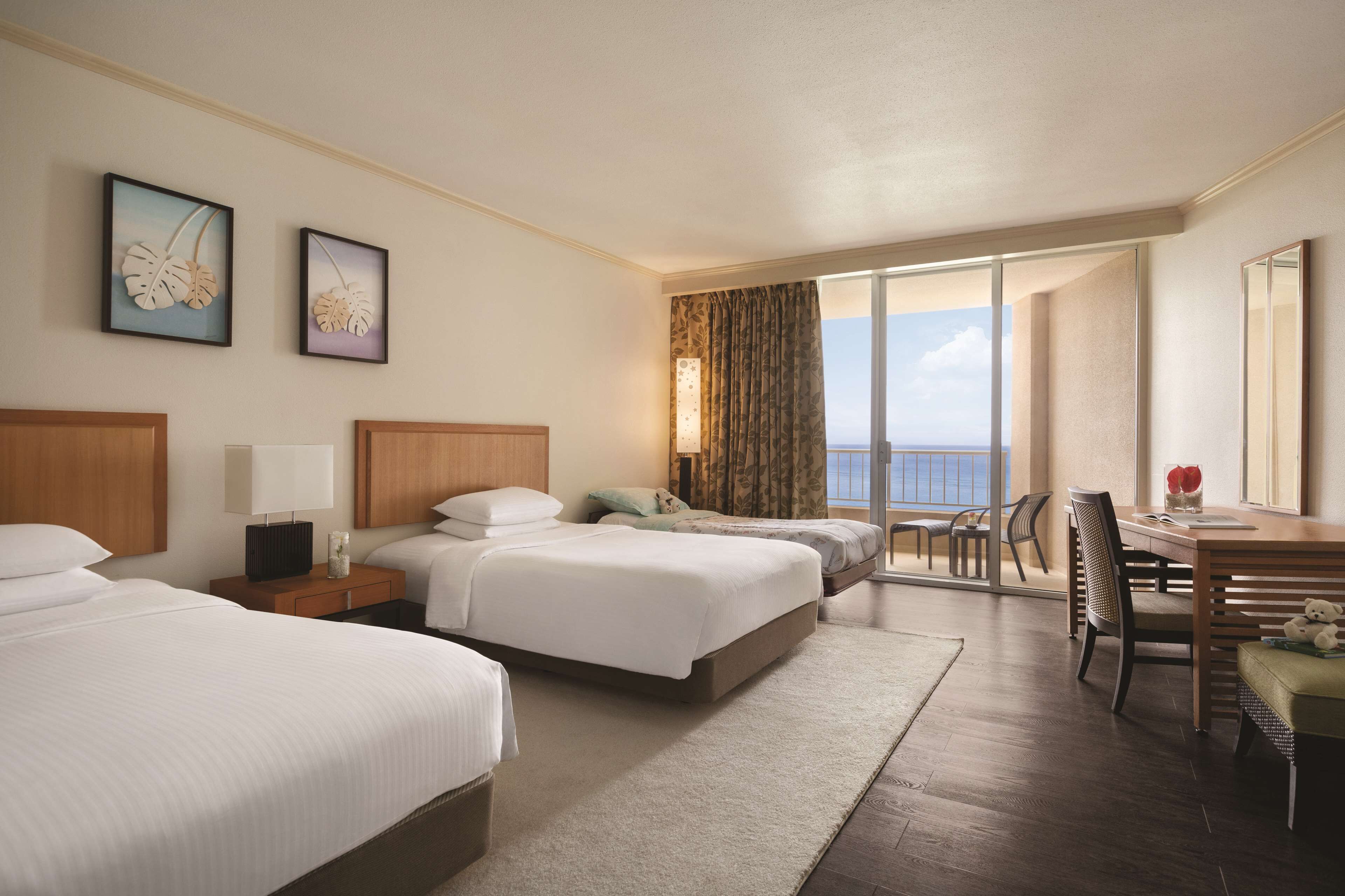 A hotel room with two beds, a dining area, and a view of the sea.