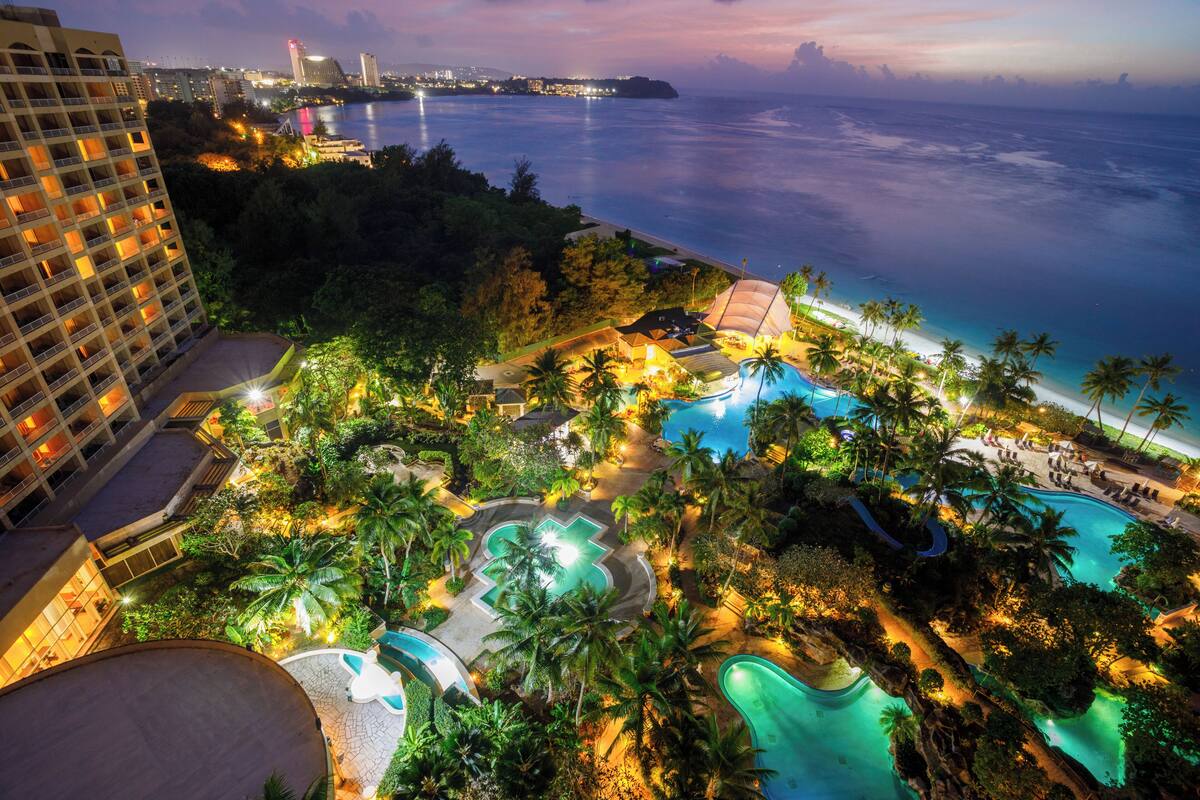 A resort with multiple swimming pools, palm trees, and a view of the ocean.