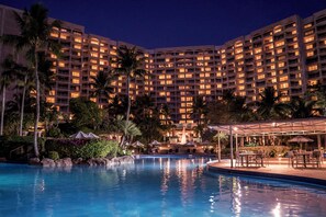A hotel with a large pool, palm trees, and a well-lit building facade.