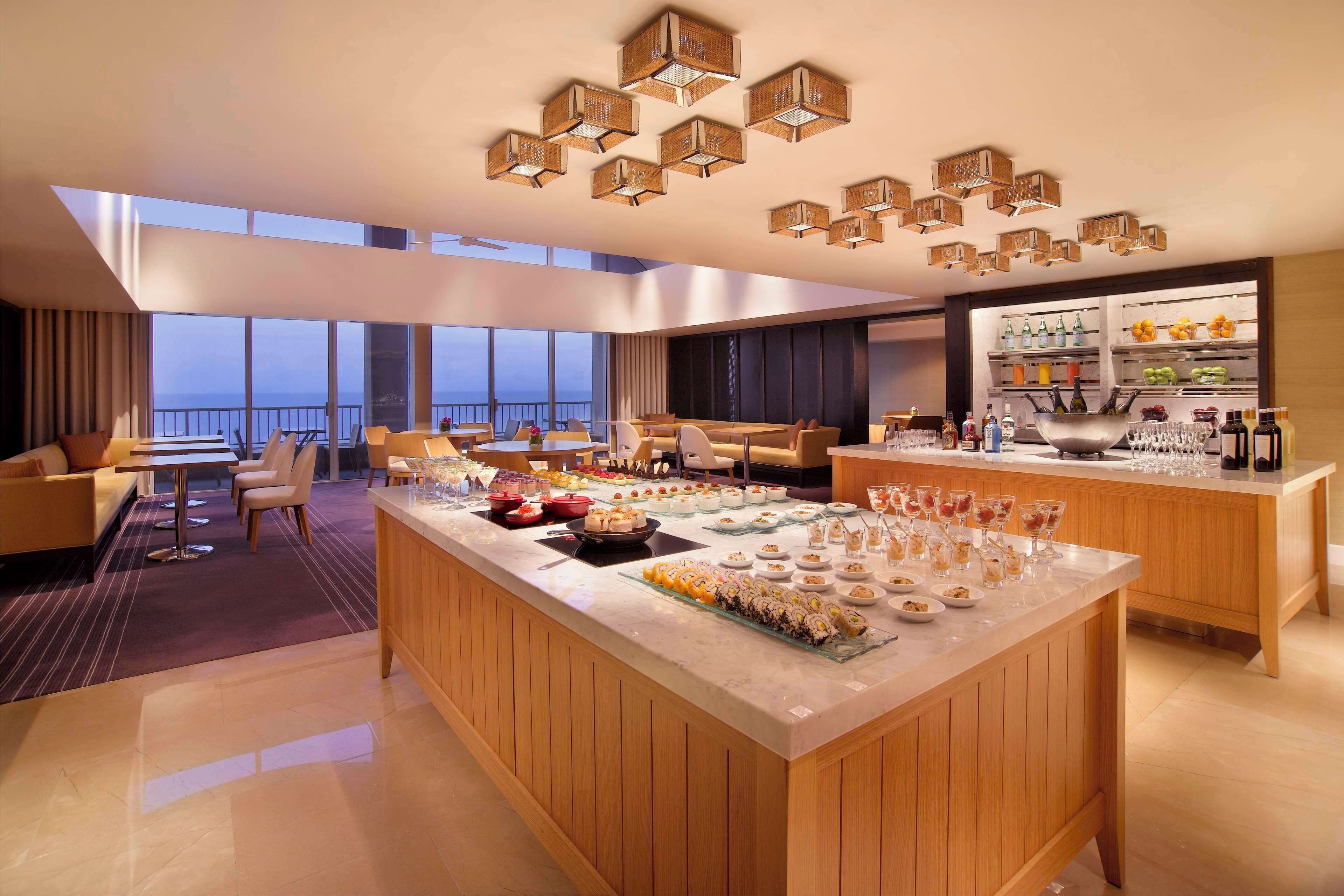 Un hall d’hôtel moderne doté d’un bar central, de différents espaces aménagés pour s’asseoir et d’un buffet.