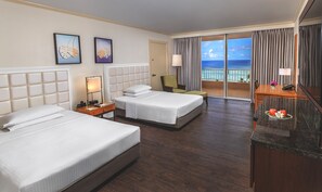 A hotel room with two beds, a desk, a chair, a nightstand, a lamp, and a view of the ocean.