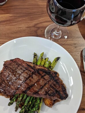 A plate with grilled steak and asparagus, and a glass of red wine on a wooden table.