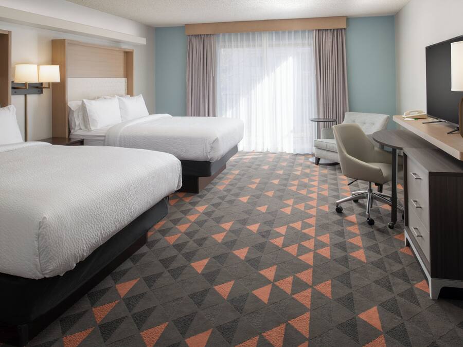 Ein Hotelzimmer mit zwei Betten, einem Schreibtisch, einem Sessel und einem Fernseher.