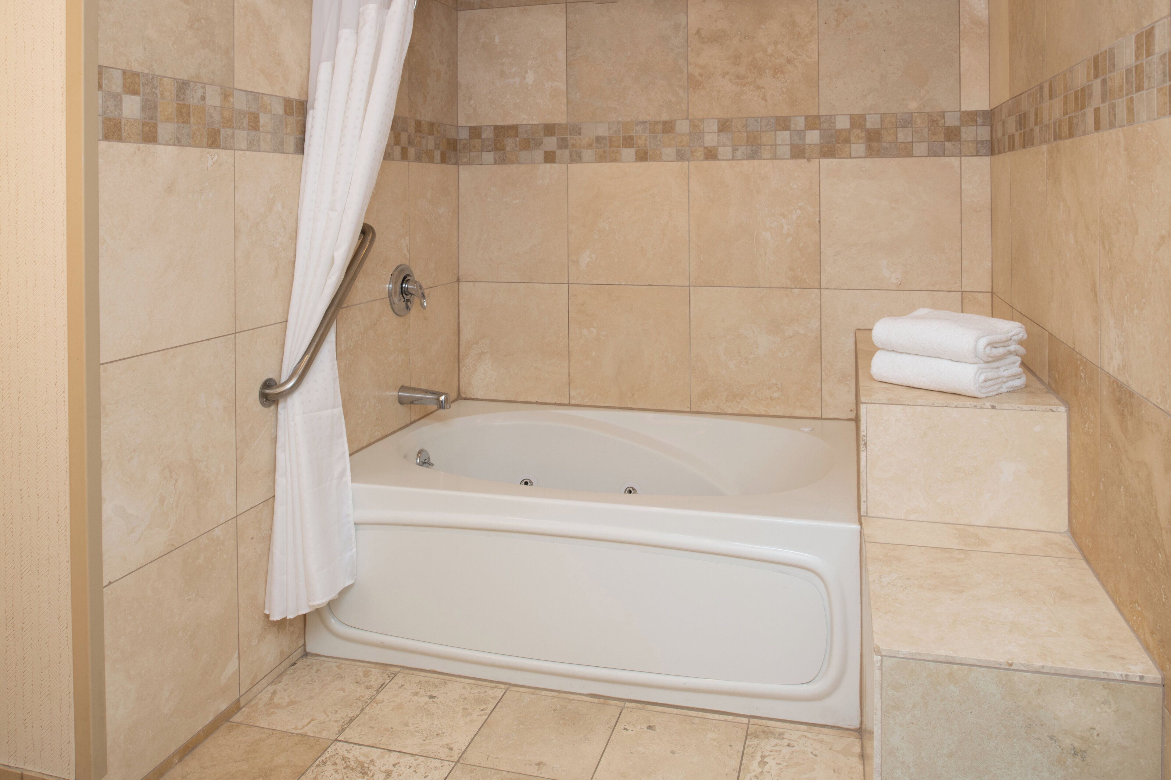 A bathroom with a bathtub, a shower curtain, and a stack of towels.