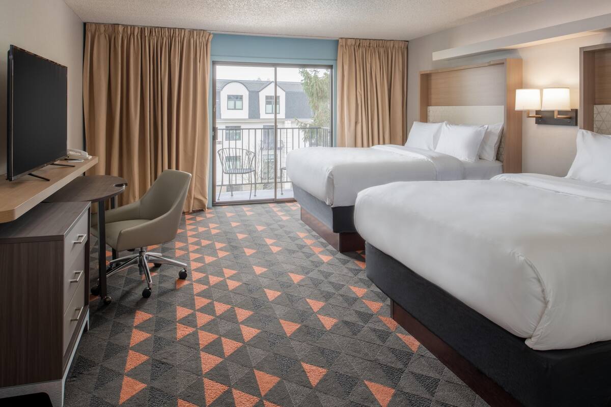 A hotel room with two beds, a desk with a TV, a chair, and a patterned carpet.