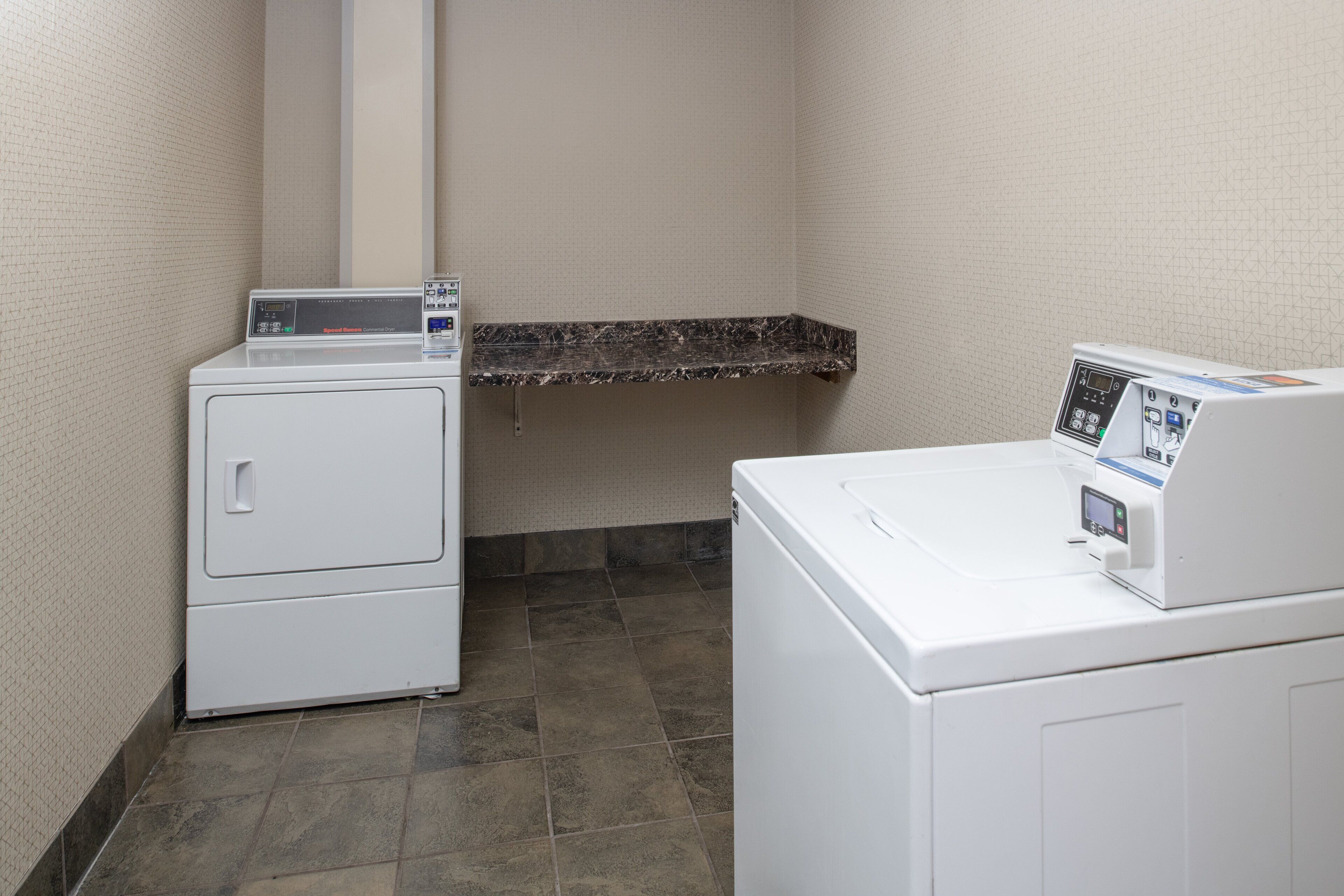 A laundry area with two white washing machines and a marble countertop.