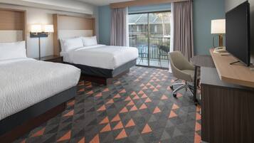 A hotel room with two beds, a desk with a TV, and a balcony with a view.
