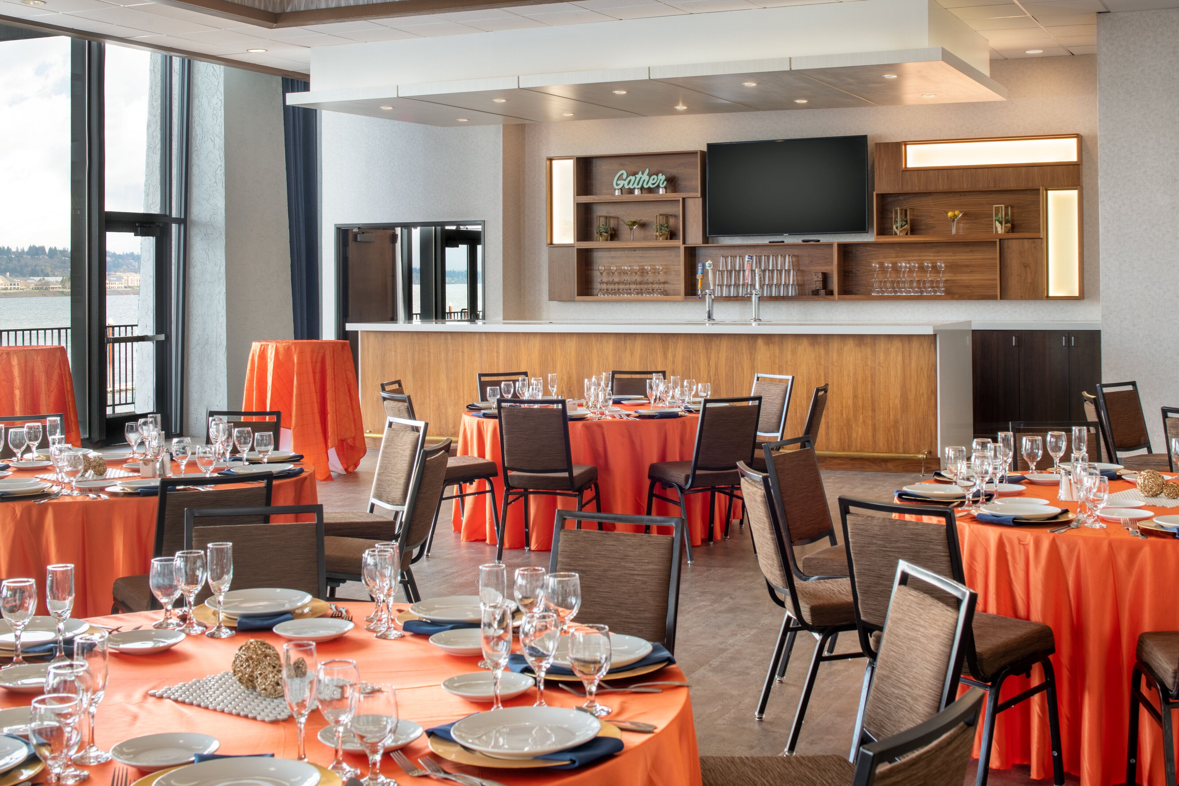 A restaurant with multiple tables set for dining, a bar area, and a large TV screen on the wall.